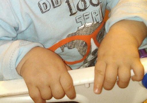 A young baby grips a high chair in anticipation of breakfast.
